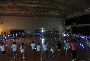 オリジナルＴシャツと光る腕輪を着用し暗闇でダンスしている様子