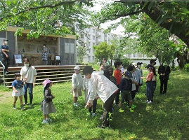 木陰で指導者とレクをする子どもたちの写真