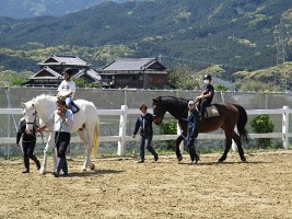 馬に乗って馬場をまわる子どもたちの写真