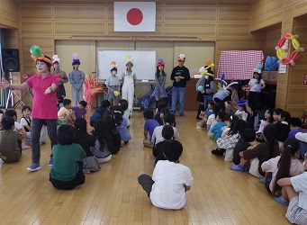 バルーンの冠を被った遊びの達人と子どもリーダーが、子ども達の前に立って紹介されています。