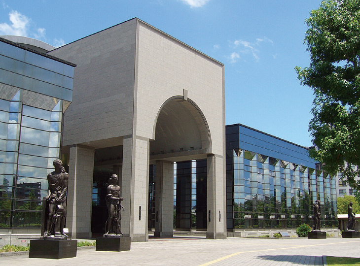 4体のブロンズ像が立っている、博物館の入口の写真。