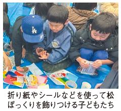 折り紙やシールなどを使って松ぼっくりを飾りつける子どもたちの写真