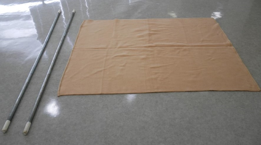 １　準備するのは毛布１枚と物干し竿などの丈夫な棒２本。毛布は摩擦抵抗の強いものを選び，棒は毛布の短辺よりも長いものを準備する。