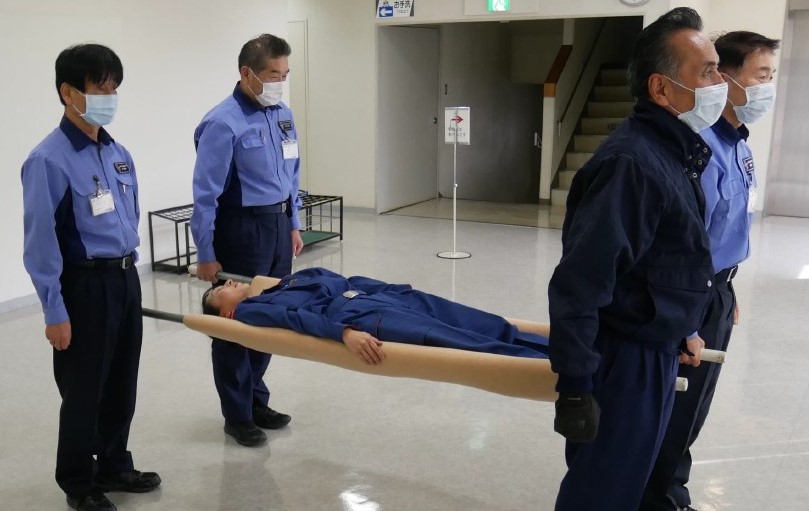 ６　傷病者を毛布の上に仰向けで寝かせ，２名から４名の搬送者がそれぞれ棒の端を持ち上げる。傷病者の足側を進行方向として搬送する。