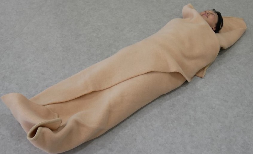 ３　傷病者の左右と足側に位置する毛布を角から折り返し，傷病者を包み込む。