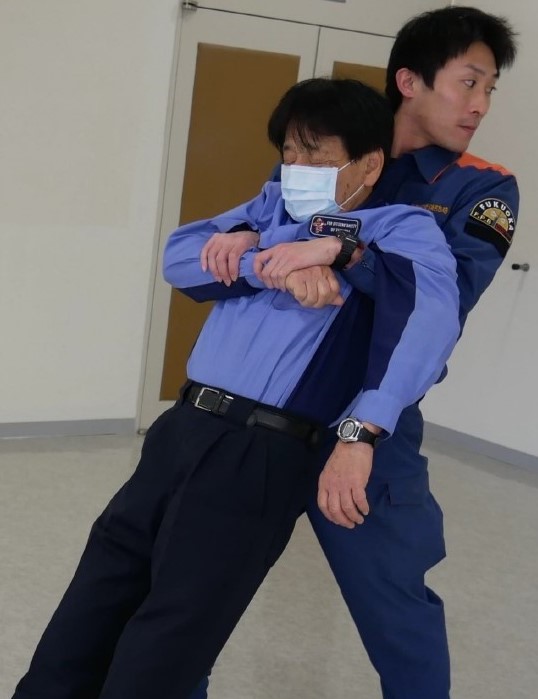 ３　搬送者は，傷病者の腕を自分の胸の前で保持したまま立ち上がり，後ろ向きに搬送する。胸の位置で保持したまま立ち上がることが困難な場合は，中腰で後方に引きずりながら搬送する。