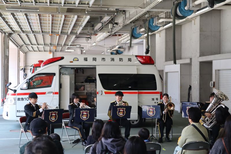 救急車の前でアンサンブル演奏を行う福岡市消防音楽隊の写真