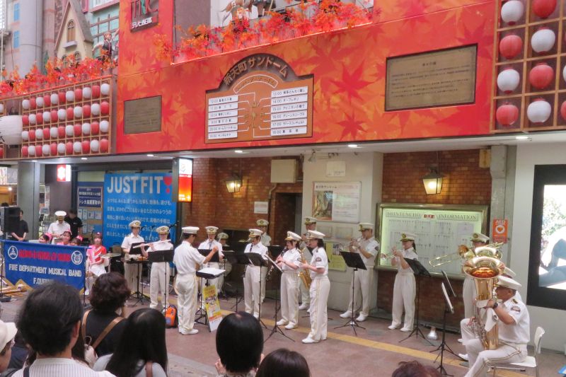 新天町のメルヘンチャイムの下で演奏を行う福岡市消防音楽隊の写真